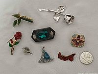 All eight brooches and pins with coin for scale