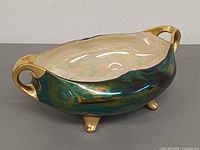 Oblique view showing green lustre exterior, cream interior, gold handles and feet
