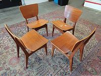Four wooden Marcel Gascoin style chairs on rug, angled view