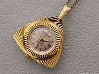 Front view of triangular gold-tone Ruby De Luxe pendant watch showing dial design and case texture