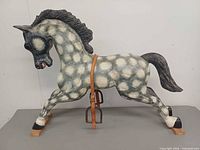 Left side view of painted wooden rocking horse showing leather strap and stirrup