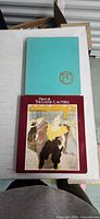 Front view showing teal hardcover and burgundy illustrated slipcase