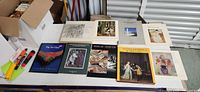 Wide shot of table displaying 11 art books with varied covers