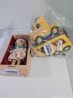 Kaloo doll in box beside sealed yellow transport truck