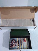 overview showing open long white box packed with cards and open green metal tin with additional cards