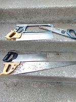 Group of five assorted hand saws displayed on concrete steps