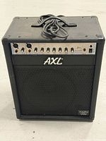 Front view of AXL B60 bass amplifier showing grille, logo and attached power cord