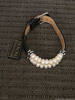Full view of bracelet showing pearls, leather strap, buckle, hang tag