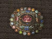 Front view of circular brooch showing central pink stone, enamel flowers and multicolored rhinestone border