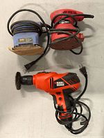 Three corded tools laid out: Black & Decker drill, blue Handi sander, red Tough sander
