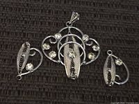 Front view of pendant and two earring drops on dark fabric background