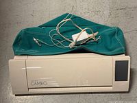 Silhouette Cameo 2 unit with teal dust cover and white AC adapter placed on top