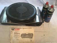Coleman Festivio stove with grill grate, two butane cans, manual