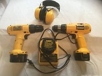 Two yellow DeWalt drills with batteries attached, DeWalt charger, yellow earmuffs
