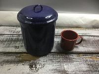 Blue speckled enamel canister with lid beside red enamel mug