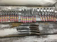 Full view of forks, table knives, spoons with matching floral handles and separate wood-handled steak knives