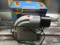 Projector unit standing beside original box with power cord visible