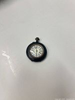 Front of pocket watch showing decorative white dial with multicolor accents, crown at 12