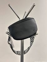 Front view of black faux leather crossbody bag on stand showing heart logo and woven strap