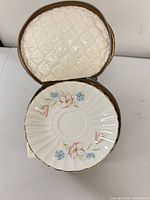 Saucer inside open padded case showing floral design and gilt rim