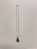 full view of silver-tone necklace with green teardrop pendant laid flat