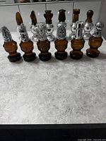Front view showing eight amber glass chess piece bottles with various silver-tone stoppers