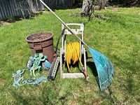 Full lot view on lawn showing reel, hose, rake, planter, sprinkler bar, metal geckos, and trellis