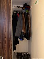 Closet view showing multiple jackets on hangers and three pairs of boots on floor