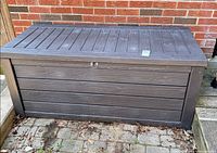 front and side view of entire resin storage deck box against brick wall