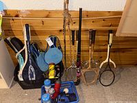 Overall lot leaning against wall with racquets, field hockey stick, paddles and baskets