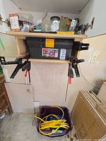 Shelf with toolbox clamped in place, bar clamps visible, extension cord in bin below