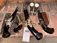 Three pistol decanters, two boot cups displayed on brick hearth