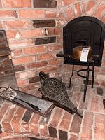 Overview of kettle on wrought iron stand, bellows, ash pan, shovel and brush on brick hearth