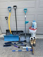 Group of shovels, brushes, ice melter tub and boots against garage door
