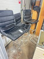 Two black bar stools side by side showing seats, backs, and chrome bases