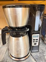 Front view of coffee maker showing carafe, brew basket, controls, stainless and black finish