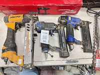 Four pneumatic staplers/nailers laid out on table