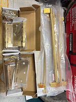 Two open Baldwin hinge boxes with hinges and screws, alongside packaged brass bar pulls