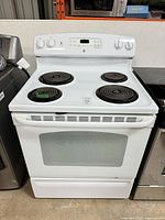 Front view of GE white electric stove showing four coil burners, oven door, storage drawer