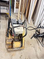 Full view of yellow plate compactor with handle and engine