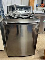 Front view of LG washing machine with hoses placed on lid