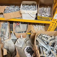Shelving section with multiple boxes and pails containing various galvanized brackets, anchor bolts, straps and plastic anchors