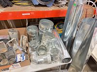 Wide shot of assorted galvanized HVAC fittings and pipes on table and two rolled sheets standing at right