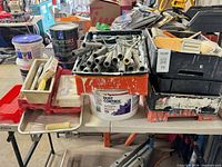 Table with roller frames in crate, paint cans, trays, buckets