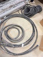 overview of large rubber hoses, flexible aluminum duct and black conduit coil on floor