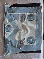Front of light blue and white Masonic apron with rosettes and tassels