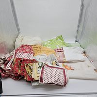 Pile of assorted patterned linens, chenille throw and curtain panel