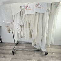 Garment rack holding lace curtain panels, crochet piece, embroidered pillowcases