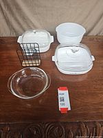 Group of ovenware items laid out: two square casseroles with lids, white bowl, clear baking dish, wire rack