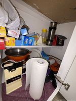 Cabinet shelf with various appliances, storage bags, saucepan, travel mug and paper towel roll